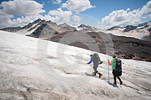 Two tourists, a man and a woman with backpacks and crampons on their feet walk along the glacier against the background