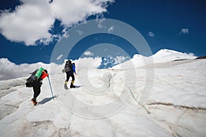 Two tourists, a man and a woman with backpacks and crampons on their feet walk along the glacier against the background
