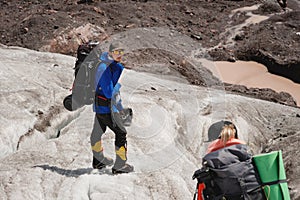 Two tourists, a man and a woman with backpacks and crampons on their feet walk along the glacier against the background