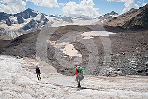 Two tourists, a man and a woman with backpacks and crampons on their feet walk along the glacier against the background