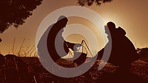 Two tourists are set the bowler cauldron on the fire lifestyle by bonfire party in nature camping silhouette sunlight