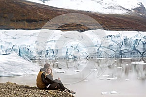 Two tourists are sitting near the glacier iceberg in Iceland