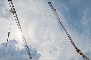 The two tower cranes and building construction site silhouette at cloudy blue and white sky and sun