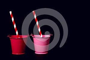 Two toy buckets on a black background with striped straws