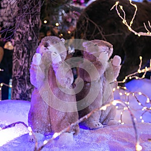 Two toy gophers with raised paws against the background of an artificial forest and snow. Christmas and New Year concept