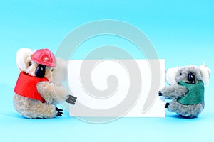 Two toy koala holding a blank white card