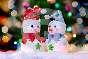 Two toy snowmen under Christmas tree on background bright bokeh _