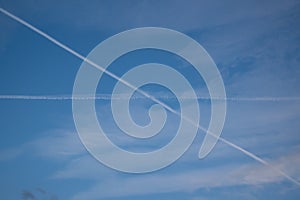 Two traces from planes crossing in the sky blue sky with some thin clouds