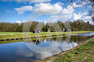 Two tractors driving on a country road along a small mill and a canal