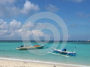 two traditional fishing boats on a beach with very clear blue sea