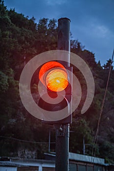 Two Traffic Light One is Lighted in Orange Signalling. Verdant Cliff and Blue Sky at Backdrop. Each Control Device has