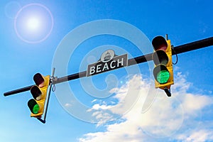 Two traffic lights and street sign BEACH. Traffic light with green light. Blue sky with sun glare