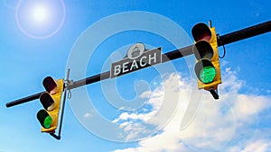 Two traffic lights and street sign BEACH. Traffic light with green light. Blue sky with sun glare,16:9