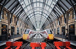 Two trains symmetrical mirrored in London Kings Cross Station deserted platforms with train waiting on each track and no passenger