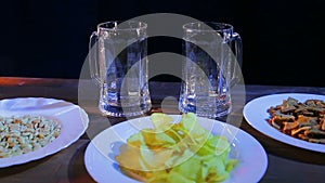 Two transparent beer mugs on a wooden table against a black background