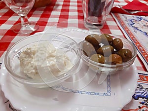 Two transparent bowls with alioli sauce and black olives on a red and white checked tablecloth