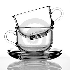 Two transparent cups on a saucer made of glass on a white background