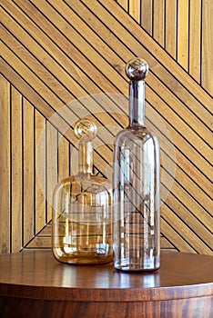 Two transparent glass decanters resting on a wooden surface, complemented by a herringbone-patterned wooden backdrop photo