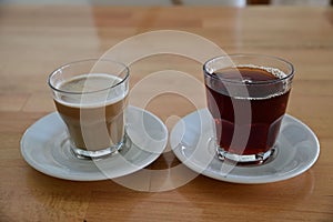 Two transparent glasses with coffee and tea on white saucers