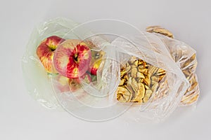 Two transparent plastic crumpled cellophane bags with groups of ripe red apples and yellow dried slices of dry apples on white bac