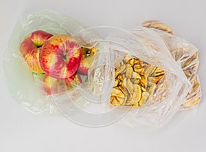 Two transparent plastic crumpled cellophane bags with ripe red apples and yellow dried slices of apples on white background. Top v