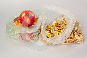 Two transparent plastic crumpled cellophane bags with ripe red apples and yellow dried slices of dry apples on white backdrop. Top