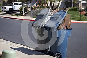 Two trashcans overflowing with trash on a suburban street