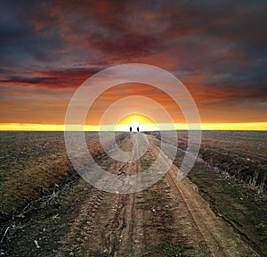 Two travelers go into the sunset distance along a field dirt road