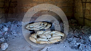 Two trays with traditional Argentinian empanadas cooking inside a clay oven.