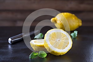 Two trendy ugly organic lemons, whole and cut, on a black table on natural wooden background. Horizontal orientation.