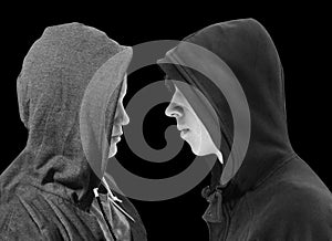 Two troubled teenage boys with black hoodie standing in front of each other in profile isolated on black background. Black and whi