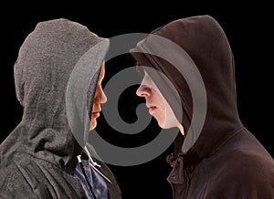 Two troubled teenage boys with black hoodie standing in front of each other in profile isolated on black background - stock