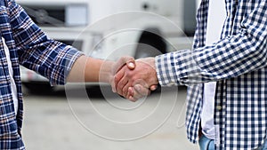 Two truck drivers shaking hands on truck parking, close up