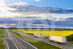 Two trucks on highway going through yelow fields