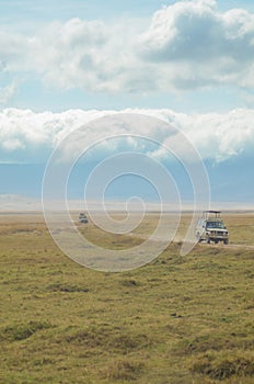 Two trucks on safari drive down a dusty dirt path in Ngorogoro Crater in Tanzania, Africa, in search of wildlife