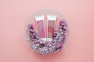 two tubes with cosmetic creams and sprigs of lilac flowers on a pink background