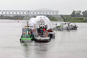 Two tugs and a barge with a large load