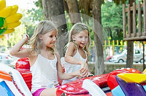 Two tween girls riding on amusement in playground in funpark