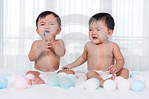 Two twin babies crying on bed
