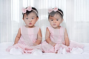 Two twin babies in pink dress on bed