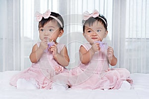 Two twin babies in pink dress on bed