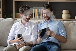 Two twin brothers sit on sofa with devices