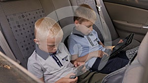 Two twin brothers are sitting in the car and playing phone and tablet.