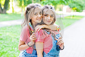 Two twin girls hugging in denim overalls with lollipops