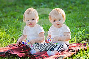 Two twin girls play with colored toys on a blanket