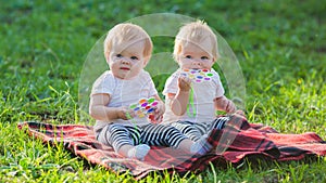 Two twin girls play with colored toys a blanket