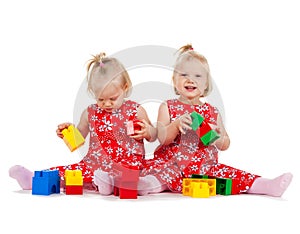 Two twin girls in red dresses playing with blocks