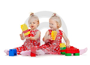 Two twin girls in red dresses playing with blocks