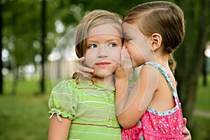 Two twin little sister girls whisper in ear photo