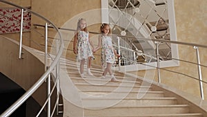 Two twin sisters in identical dresses descend the marble staircase in the hotel.